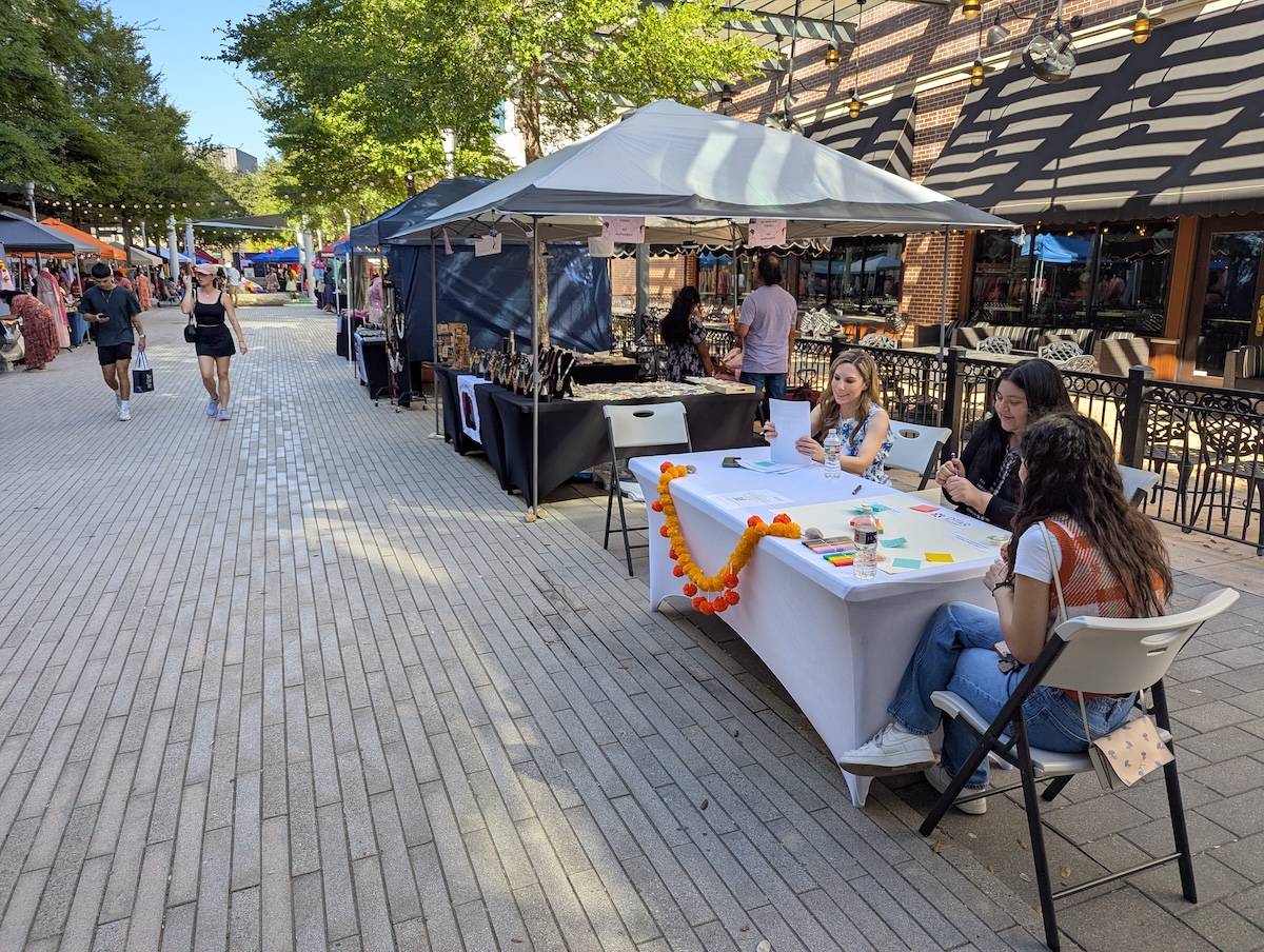 Wide view of the community market showing DTAR table among other vendors in a vibrant outdoor setting